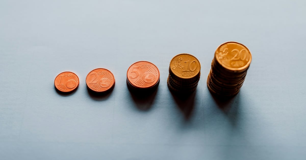 Copper coins set out in a row on a gray surface, from a single coin to a small stack