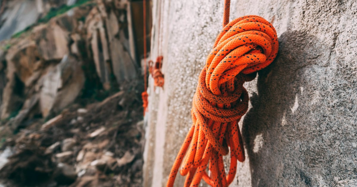 A coiled orange climbing rope hanging from an anchor on a pale rock wall