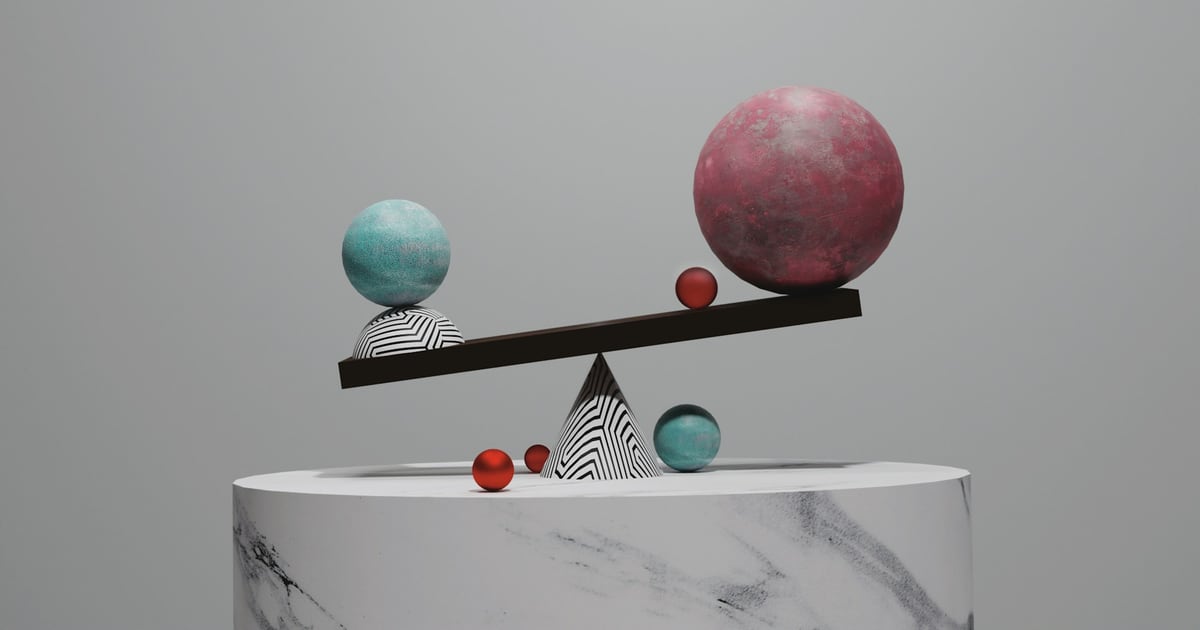 A plank balanced on a striped cone, a small blue sphere on one end and a large pink sphere on the other
